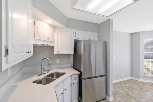 kitchen featuring white cabinets, light countertops, freestanding refrigerator, and a sink