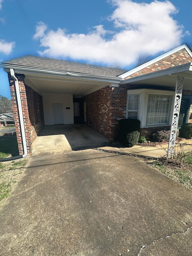 view of front facade featuring a carport, brick siding, driveway, and a shingled roof