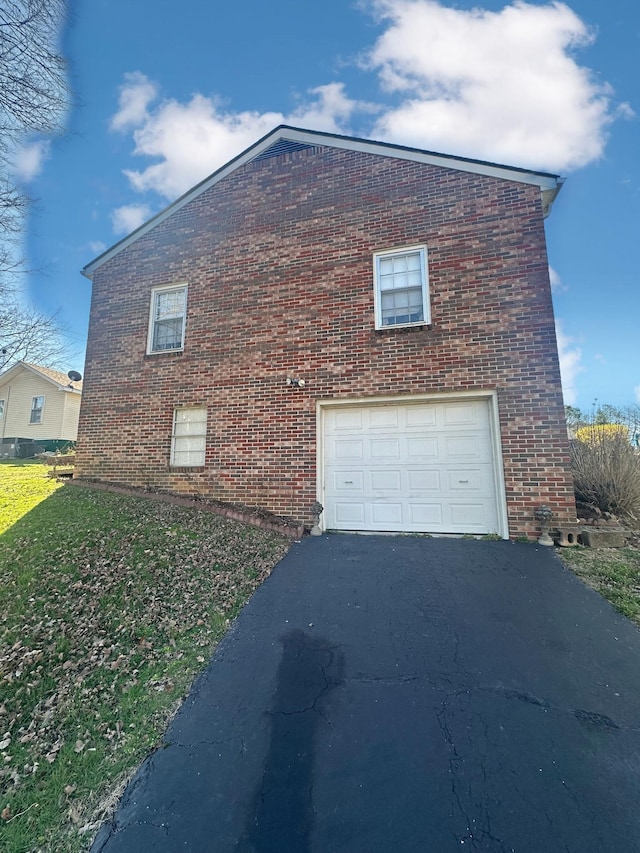 view of side of home featuring aphalt driveway, an attached garage, a lawn, and brick siding