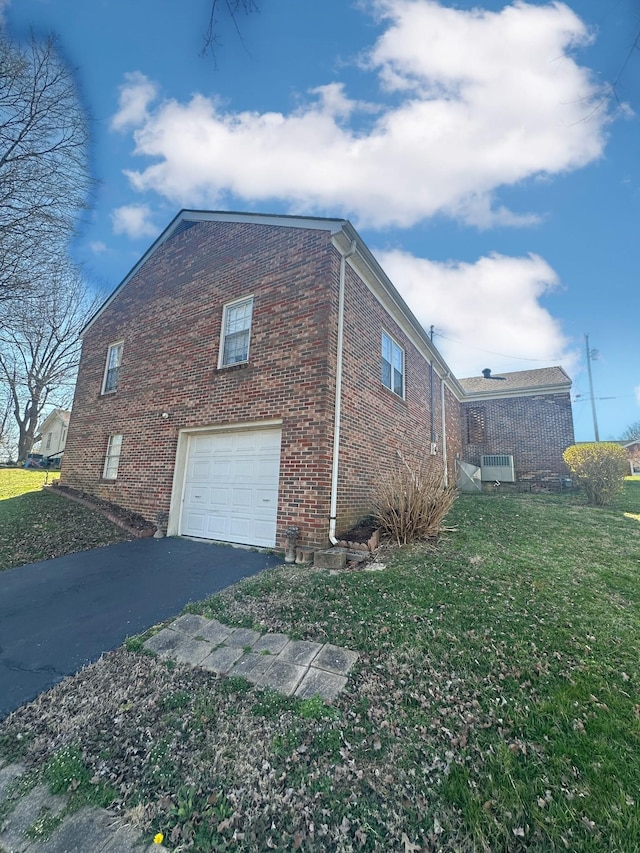 view of side of home featuring brick siding, a yard, driveway, and a garage