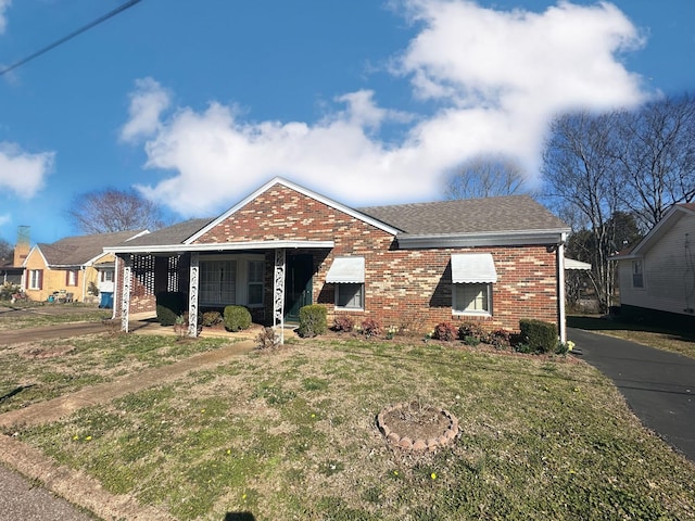 view of front of home featuring brick siding, a front yard, and a shingled roof