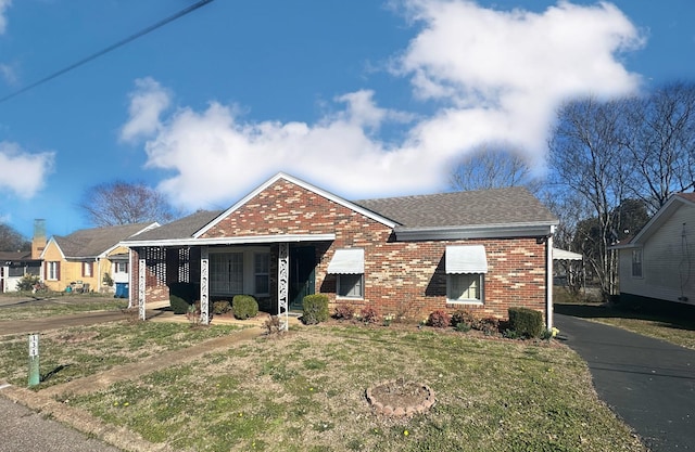 view of front of house featuring brick siding, a front yard, and a shingled roof