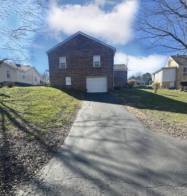 view of side of property featuring a garage, aphalt driveway, a yard, and brick siding