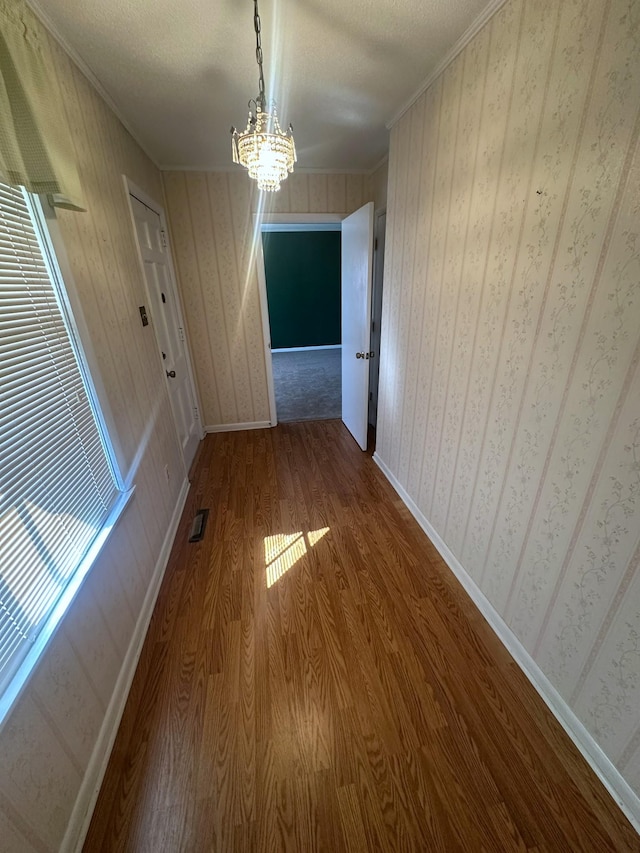 unfurnished dining area with visible vents, wallpapered walls, baseboards, ornamental molding, and wood finished floors