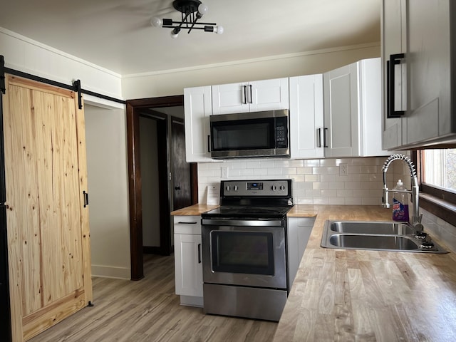 kitchen with a sink, stainless steel appliances, white cabinets, a barn door, and tasteful backsplash