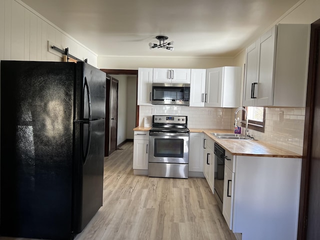 kitchen with a sink, black appliances, light wood-style floors, tasteful backsplash, and butcher block counters