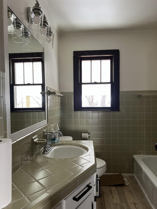 full bath with toilet, a tub, wood finished floors, tile walls, and vanity