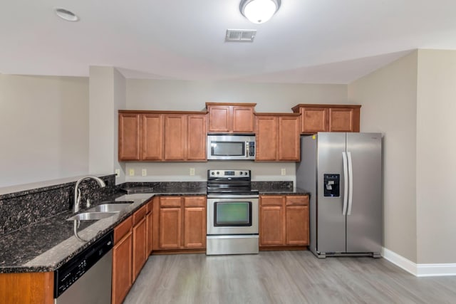 kitchen featuring visible vents, brown cabinets, a sink, dark stone counters, and appliances with stainless steel finishes