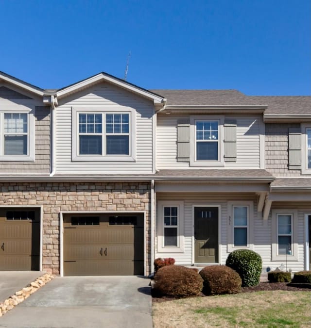 townhome / multi-family property with concrete driveway, a garage, stone siding, and a shingled roof