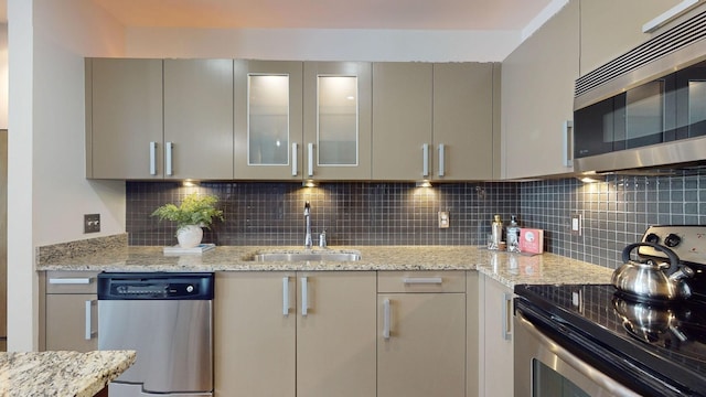 kitchen featuring gray cabinetry, a sink, backsplash, appliances with stainless steel finishes, and glass insert cabinets