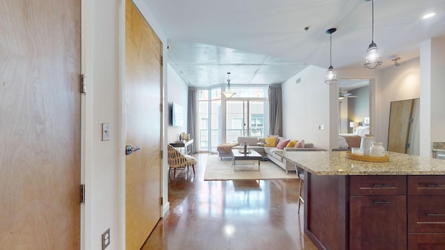 kitchen featuring decorative light fixtures, light stone countertops, open floor plan, and concrete floors