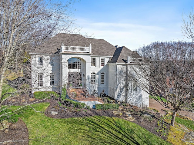 view of front of home featuring a shingled roof, a front lawn, a balcony, and stucco siding