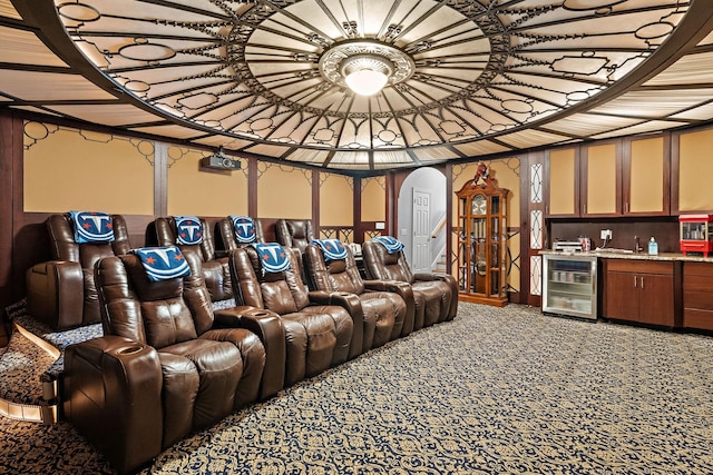 home theater room featuring wine cooler, light colored carpet, arched walkways, and indoor wet bar