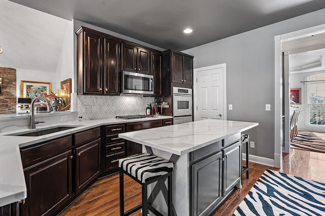 kitchen with dark wood-style floors, stainless steel appliances, a sink, a kitchen bar, and backsplash