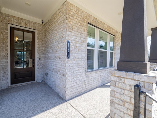 view of exterior entry with brick siding and a porch