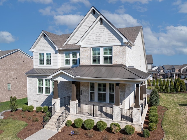 craftsman house with a standing seam roof, a porch, a front yard, metal roof, and brick siding