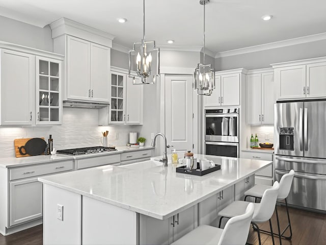 kitchen featuring a kitchen island with sink, a sink, appliances with stainless steel finishes, a breakfast bar area, and white cabinets