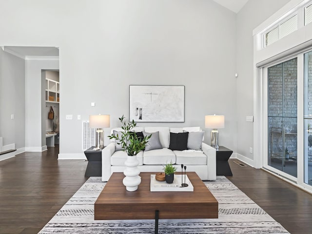 living room featuring visible vents, ornamental molding, dark wood-style floors, a high ceiling, and baseboards