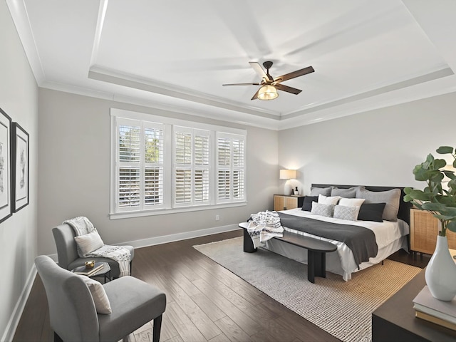 bedroom with crown molding, baseboards, wood finished floors, a raised ceiling, and a ceiling fan