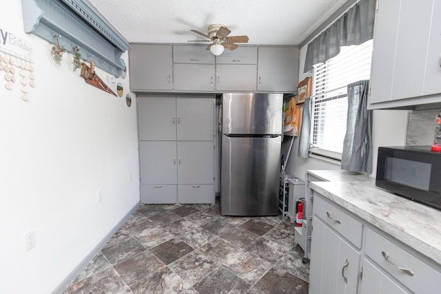 kitchen with a ceiling fan, freestanding refrigerator, light countertops, black microwave, and a textured ceiling