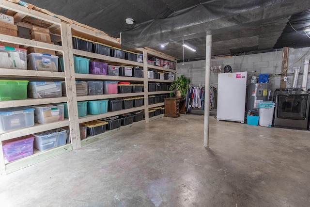 basement with water heater, concrete block wall, and white refrigerator