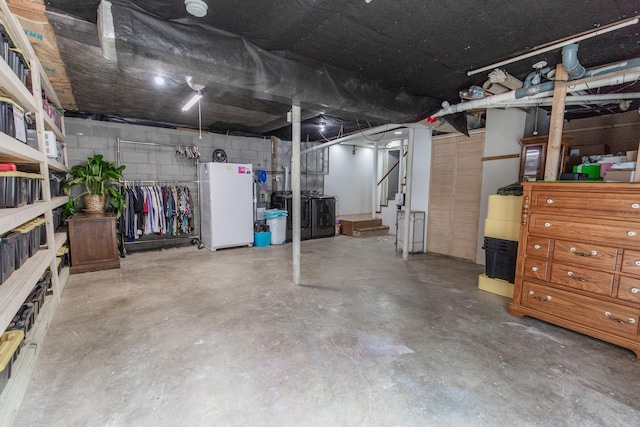 basement featuring concrete block wall and freestanding refrigerator