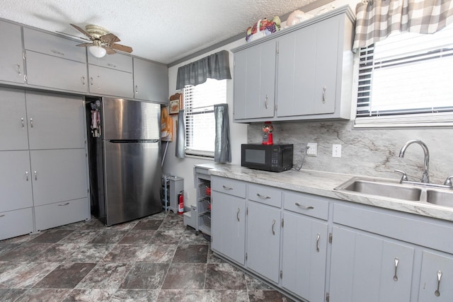 kitchen featuring gray cabinetry, a sink, tasteful backsplash, freestanding refrigerator, and black microwave