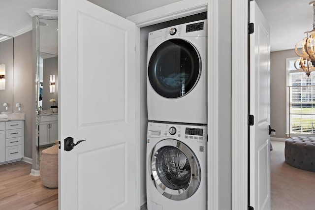 washroom featuring light wood-style flooring, stacked washer and dryer, a chandelier, and laundry area