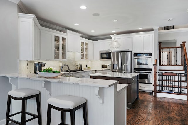 kitchen featuring glass insert cabinets, dark wood finished floors, light stone counters, appliances with stainless steel finishes, and a peninsula