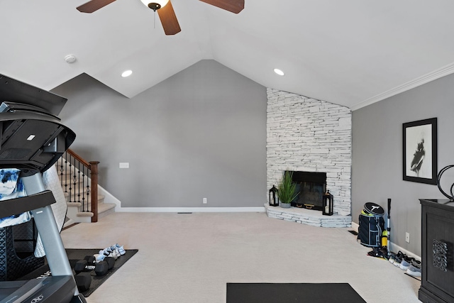 workout area featuring a ceiling fan, carpet, a stone fireplace, baseboards, and vaulted ceiling