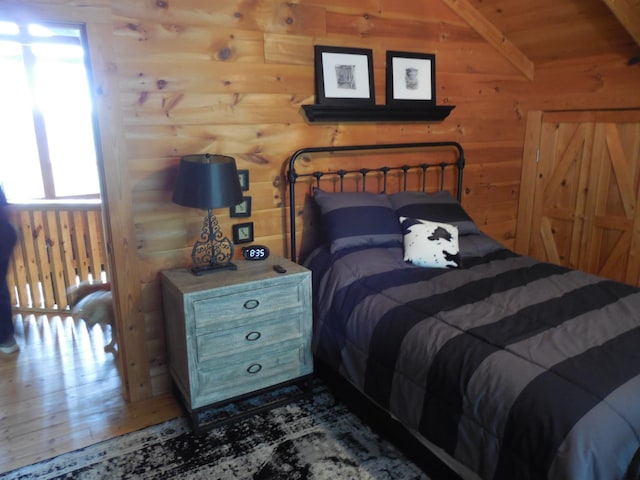 bedroom with lofted ceiling, wooden walls, and wood finished floors