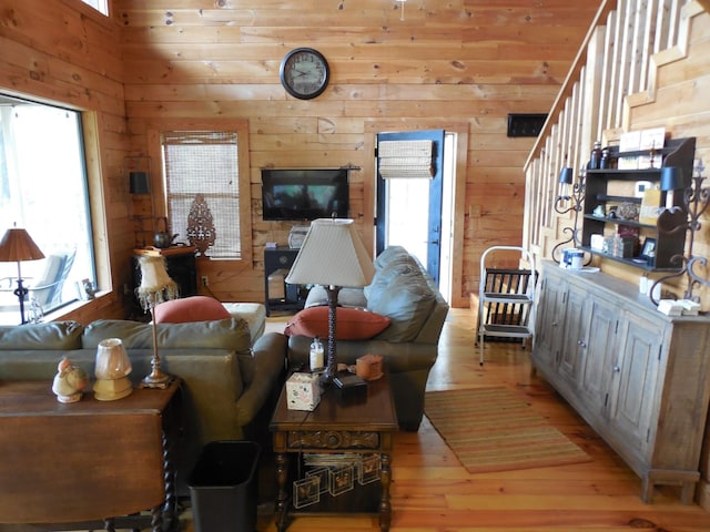 living room featuring light wood-style flooring, stairs, and wood walls