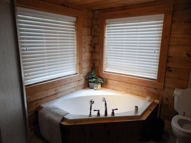 bathroom featuring plenty of natural light, toilet, a bath, and wood walls