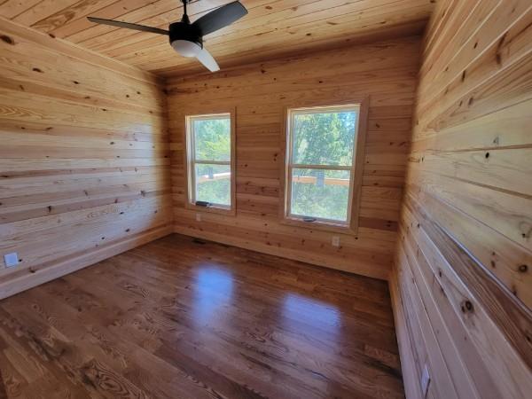 unfurnished room featuring a ceiling fan, wood finished floors, wood ceiling, and wood walls