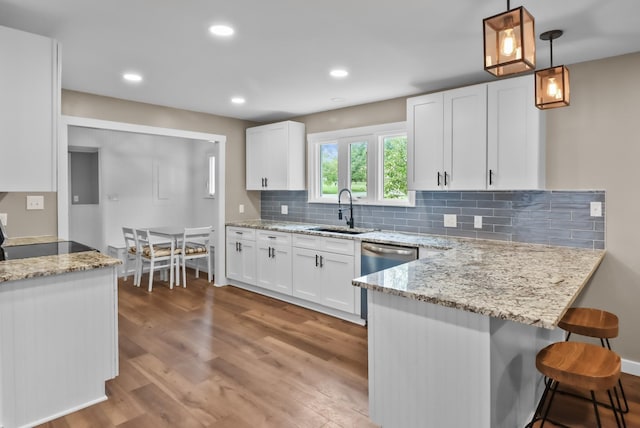 kitchen with a sink, white cabinetry, light wood-style floors, a peninsula, and light stone countertops