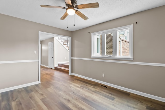 unfurnished room featuring visible vents, ceiling fan, baseboards, stairway, and wood finished floors