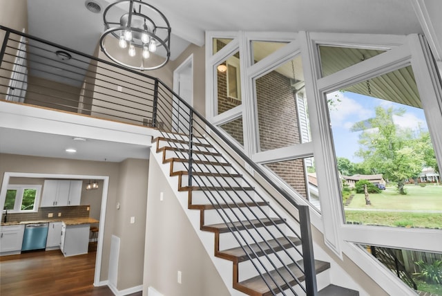 stairs with an inviting chandelier, wood finished floors, and a healthy amount of sunlight