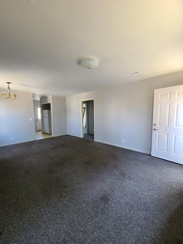 empty room featuring baseboards, a notable chandelier, and dark carpet