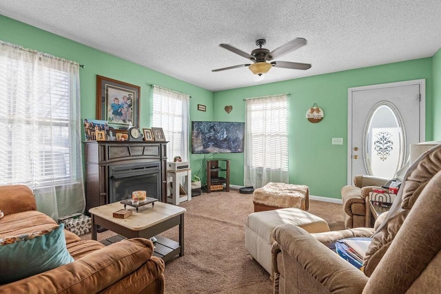 carpeted living room with a glass covered fireplace, ceiling fan, a textured ceiling, and baseboards