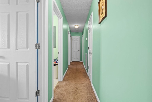 hall with a textured ceiling, baseboards, and light carpet