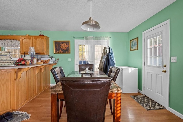 dining room featuring light wood finished floors, a textured ceiling, and baseboards