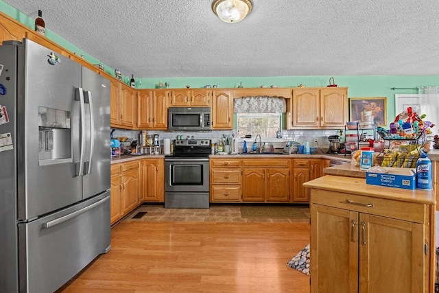 kitchen with a sink, light countertops, appliances with stainless steel finishes, light wood-type flooring, and backsplash