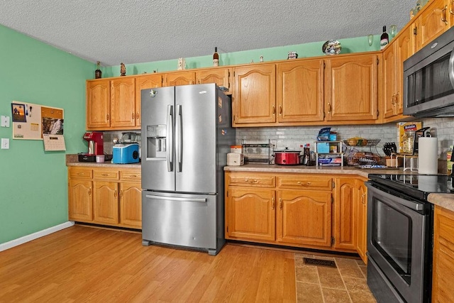 kitchen with backsplash, appliances with stainless steel finishes, and light wood-type flooring