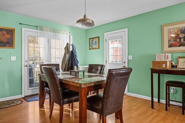 dining area featuring light wood-style flooring, a textured ceiling, and baseboards