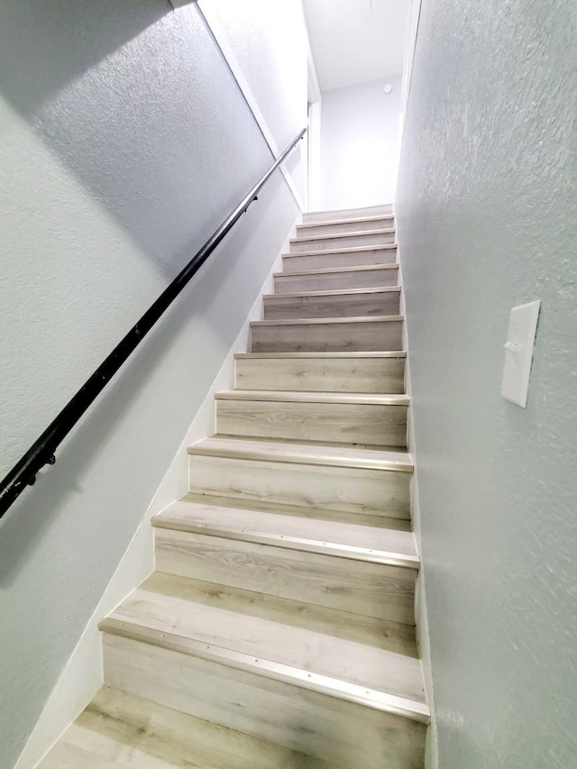 stairway featuring wood finished floors and a textured wall