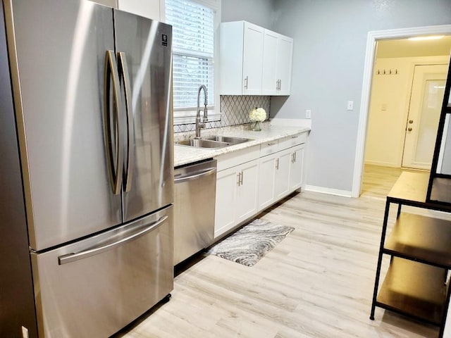 kitchen featuring light wood finished floors, light countertops, decorative backsplash, appliances with stainless steel finishes, and a sink