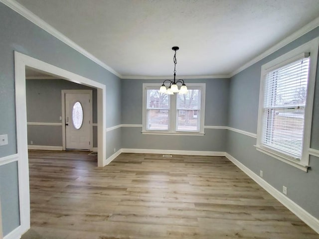 unfurnished dining area with a chandelier, crown molding, baseboards, and wood finished floors