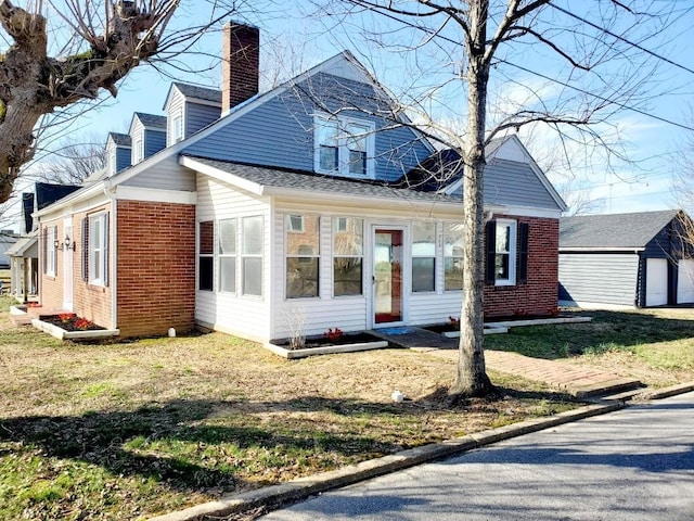 view of front of house featuring a front yard, brick siding, an outdoor structure, and a chimney