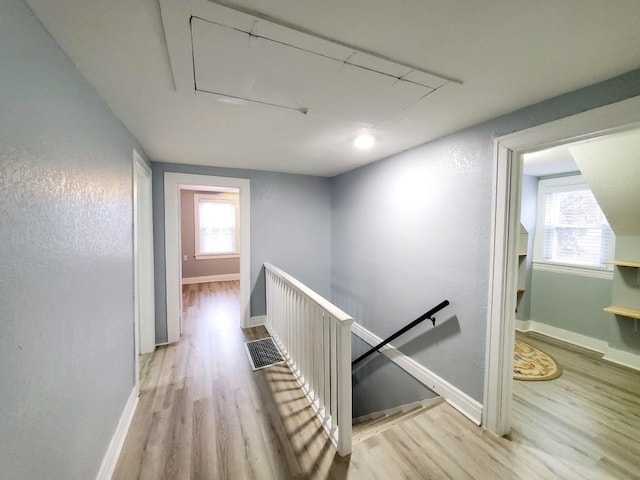 hallway featuring wood finished floors, plenty of natural light, and an upstairs landing