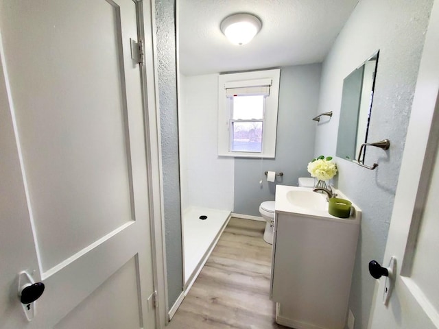 bathroom featuring toilet, wood finished floors, a shower stall, baseboards, and vanity